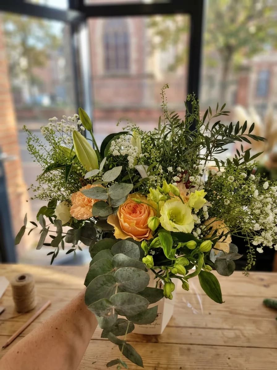 Bouquet aux fleurs pêche et crème, feuillages verts et eucalyptus, photographié dans un atelier lumineux
