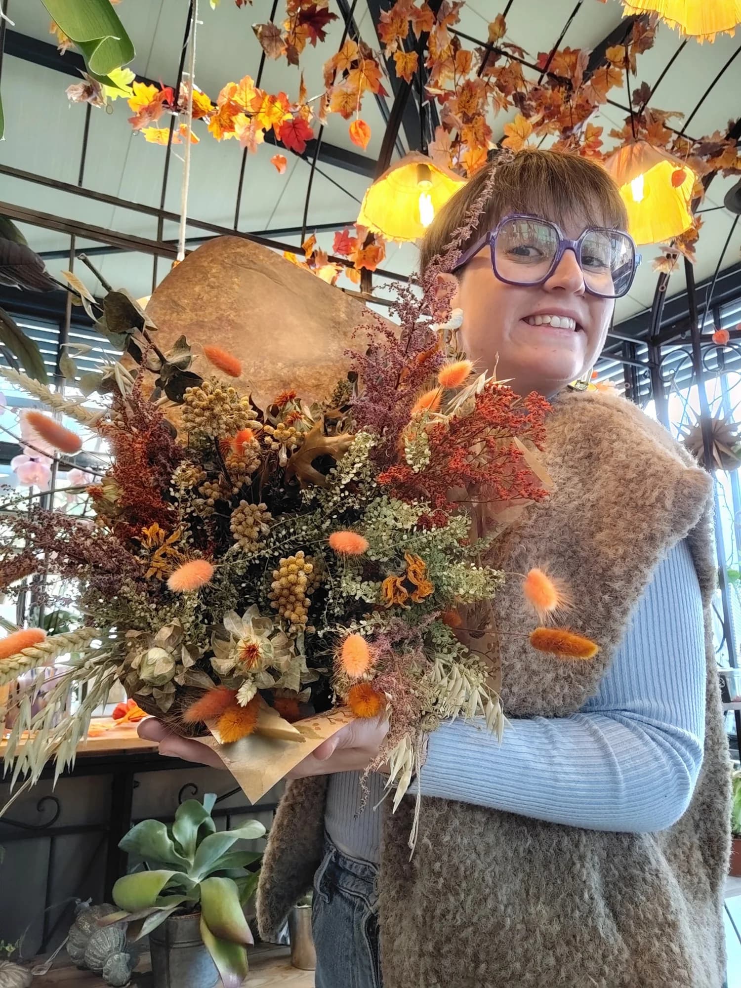 Cathy tient une grande composition de fleurs séchées dans des tons rouille, orange et beige