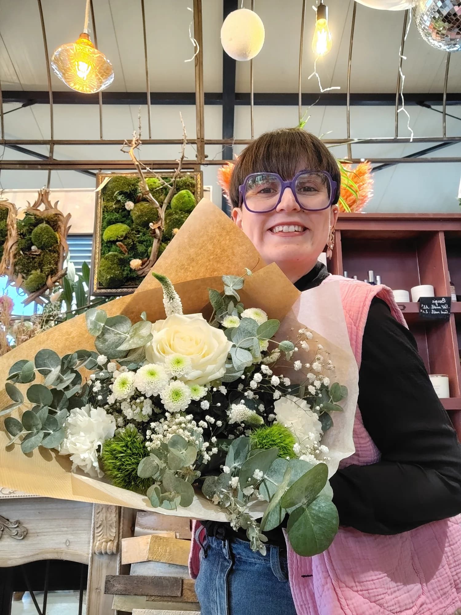 Cathy souriante tient un grand bouquet blanc et vert composé autour d'une rose blanche centrale