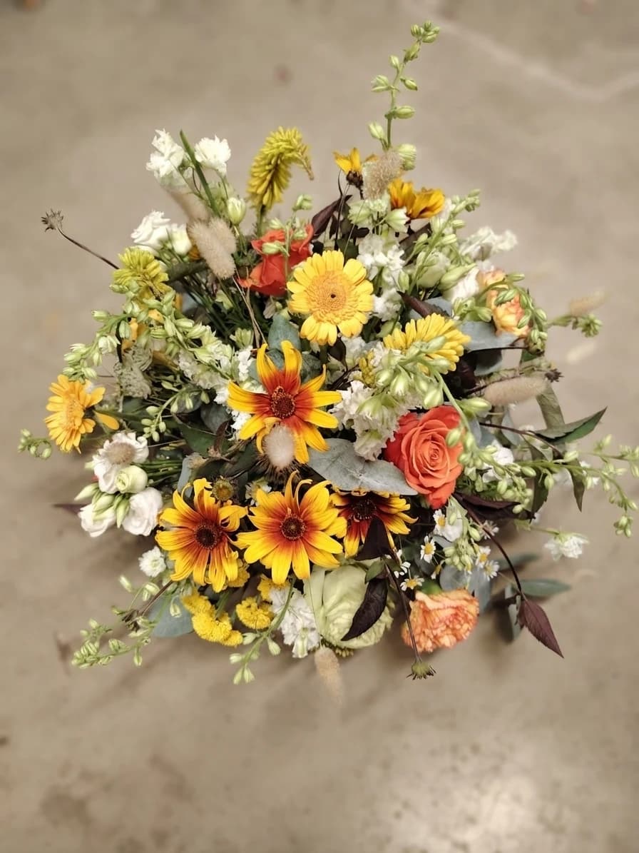 Composition de deuil champêtre et lumineuse, mêlant fleurs jaunes, orange, blanches et feuillages verts